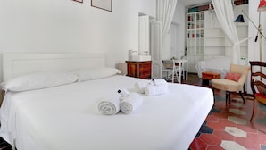 A hotel room with a large bed, white curtains, a bookshelf, a desk, and a chair. - Charming Colosseum (Rome)