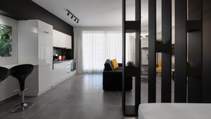 Eine moderne Küche mit weißen Schränken, schwarzen Barhocker und einer großen Wandkunst mit grünen Blättern.