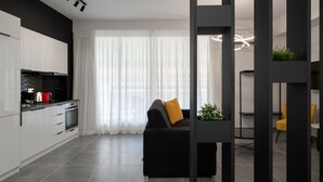 Eine moderne Küche mit weißen Schränken, ein schwarzes Sofa mit einem senffarbenen Kissen und ein Essbereich mit gelben Stühlen.