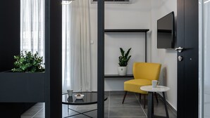 Ein modernes Hotelzimmer mit einem gelben Sessel, einem kleinen runden Tisch, einer Topfpflanze und einem an der Wand befestigten Fernseher.