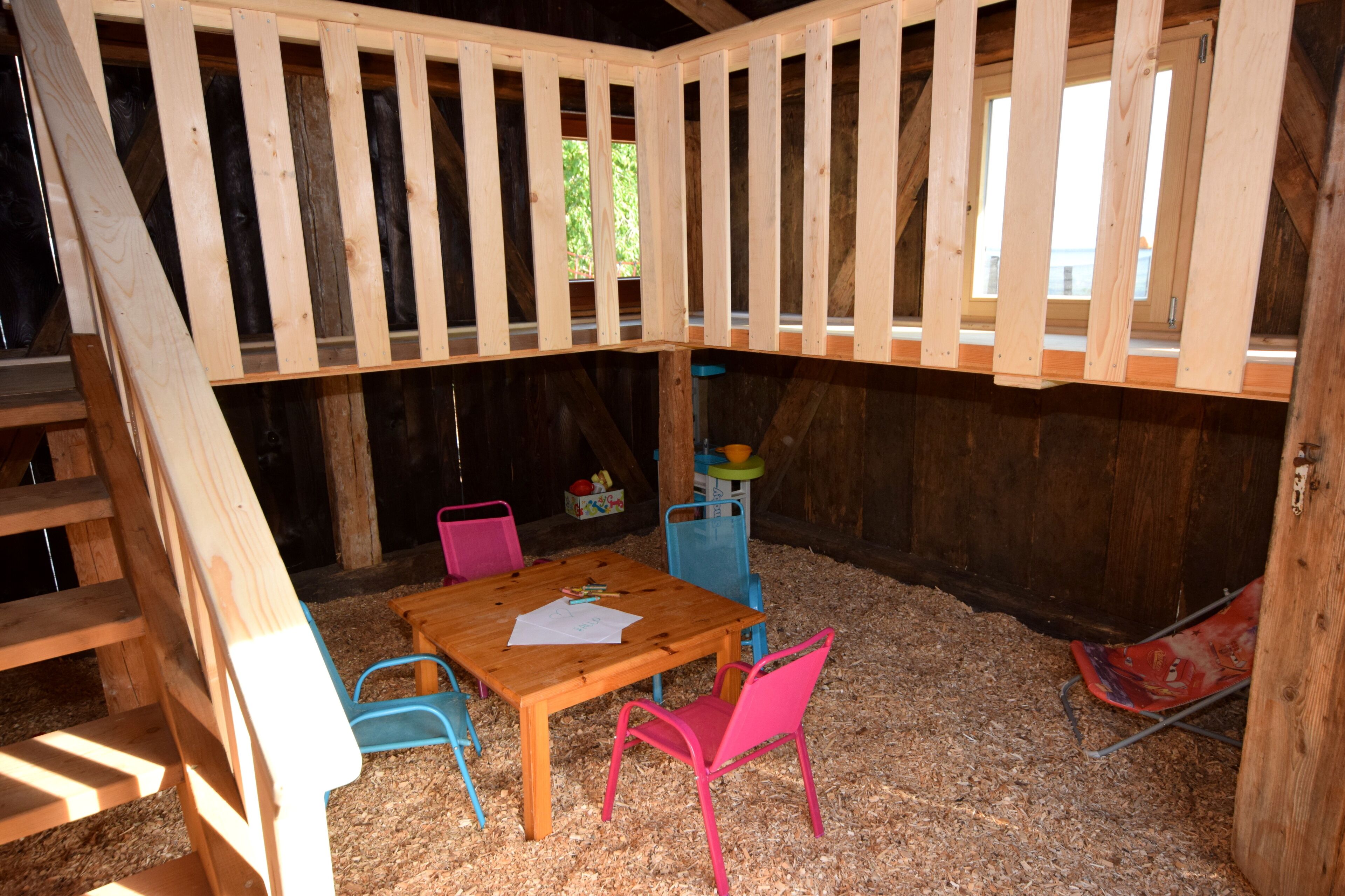 Um espaço de brincadeiras de madeira com mesa, cadeiras, uma escada e uma janela.