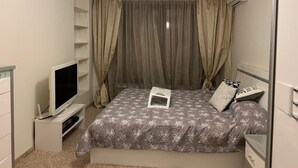 Een slaapkamer met een bed, een televisie op een dressoir, een nachtkastje en een kledingkast.