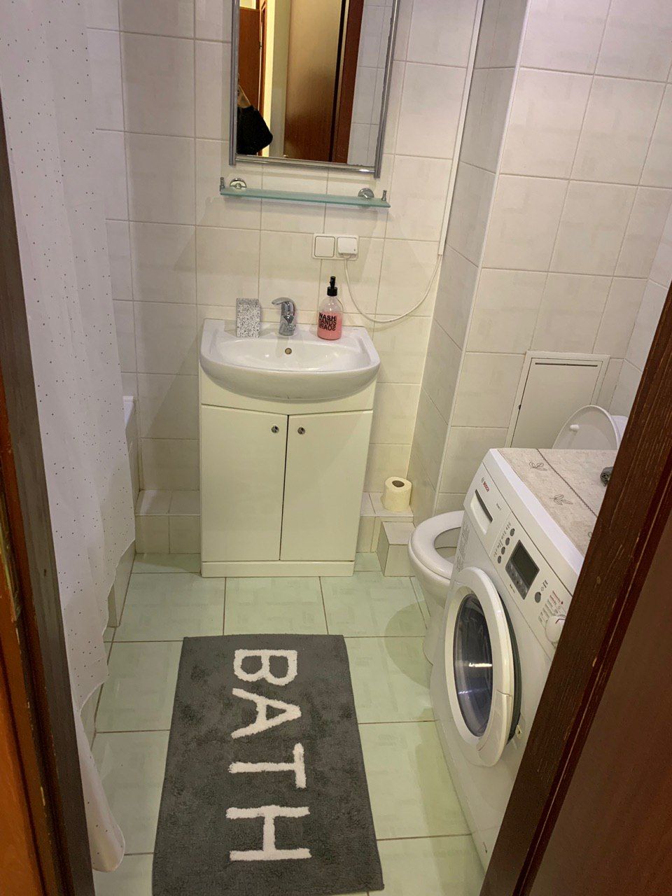 A small bathroom with a sink, mirror, and a washing machine.