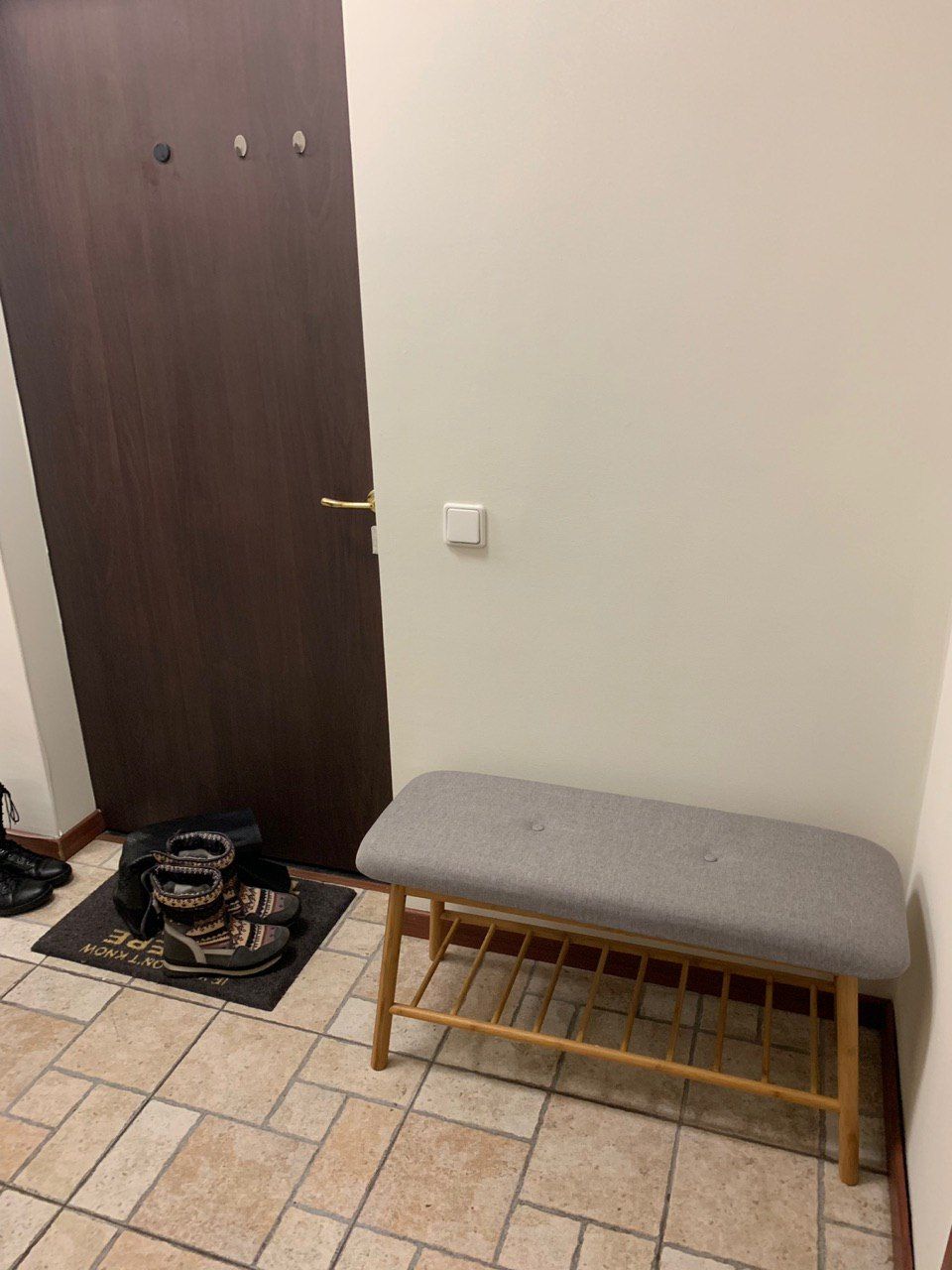A bench in a room with a tiled floor, a door, and a wall-mounted light switch.