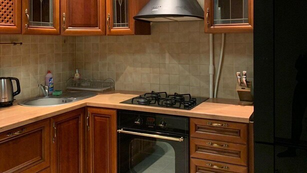 Een keuken met houten kastjes, een gasfornuis, een oven en een zwarte koelkast.