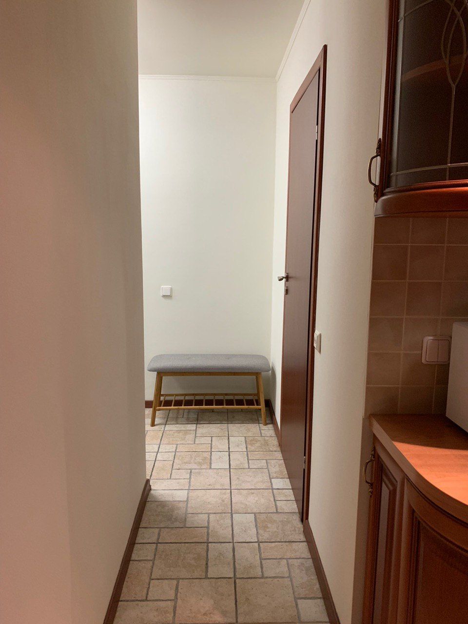 Un pasillo estrecho con un banco, una puerta y una zona de cocina con armarios.