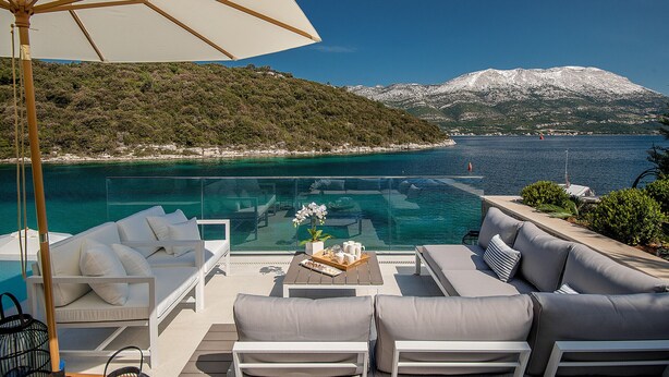 Un espace extérieur luxueux, aménagé avec un coin salon, une piscine, des meubles blancs et une vue sur les montagnes.