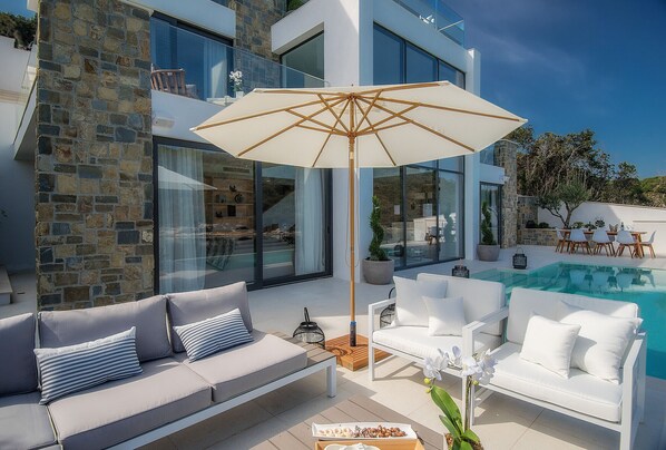 A modern outdoor seating area with a pool, stone walls, and a large umbrella. - Luxury Villa Korcula Supreme (Korcula)