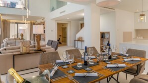 Un coin repas avec une table en bois dressée pour six personnes, entourée de chaises modernes. Un escalier mène à l’étage supérieur.
