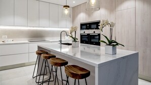 Une cuisine moderne dotée d’un grand îlot central, de tabourets de bar, de luminaires suspendus et d’un four à micro-ondes.