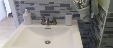 A bathroom with a white sink, a towel rack, and a tiled backsplash.