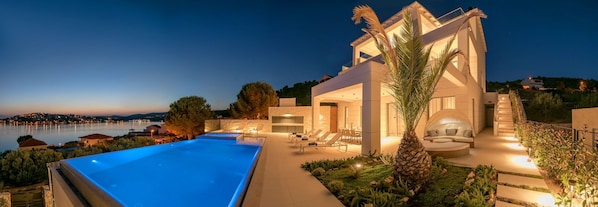A modern villa with a swimming pool, outdoor seating, and a view of the sea.