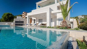 A modern poolside area with clear blue water, lounge chairs, and a white building with balconies. - Luxury Villa Carpe Diem Paradise (Rogoznica)