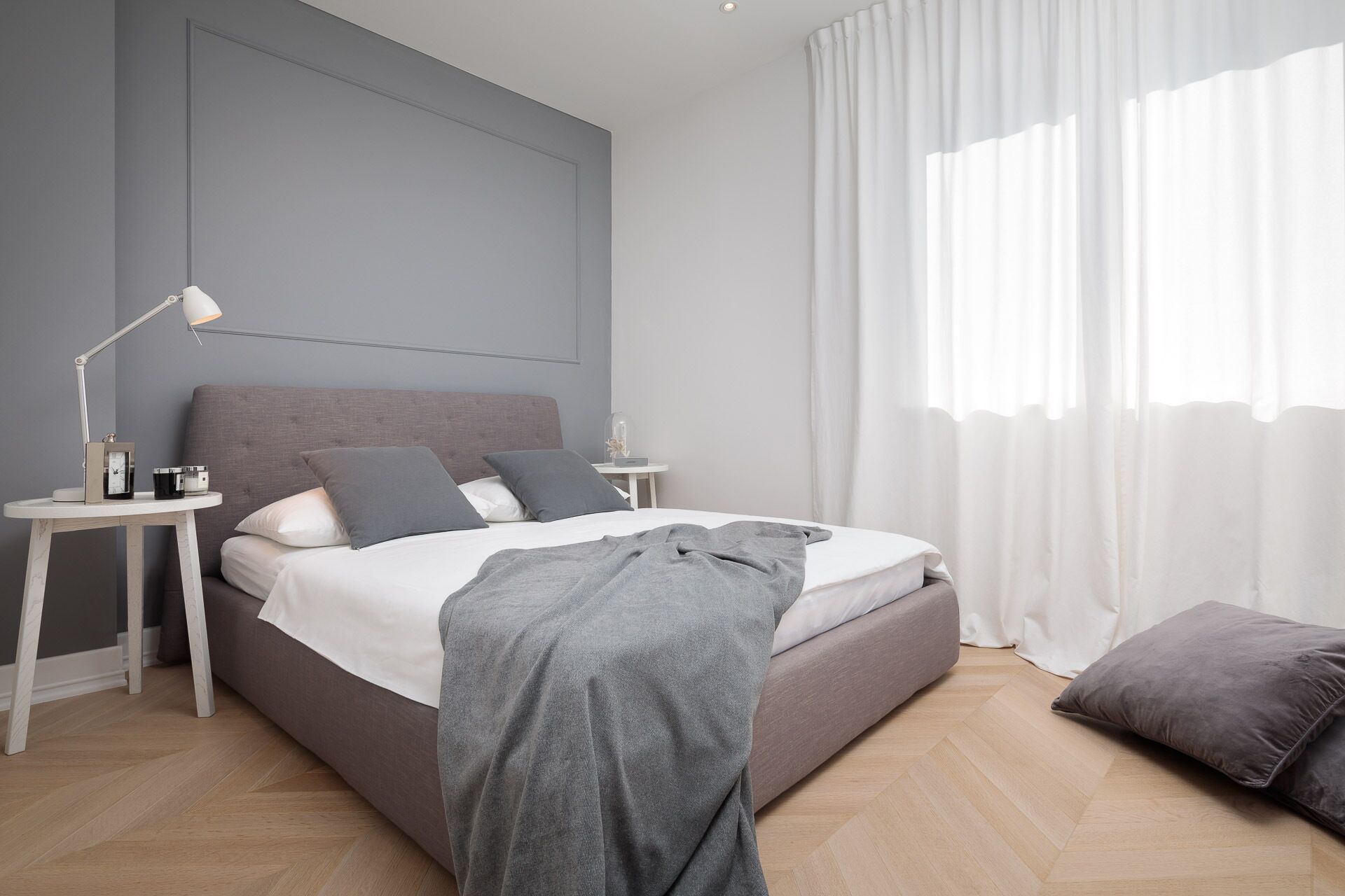 A modern bedroom with a bed, bedside tables, a lamp, and a window with curtains.
