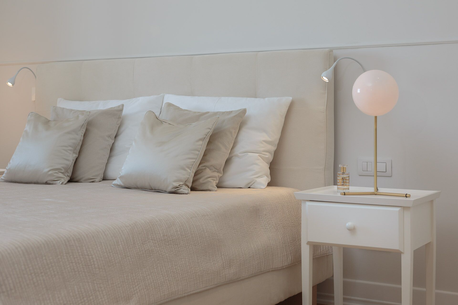 Un lit bien fait, avec une tête de lit et des oreillers de couleur claire, une table de chevet avec une lampe et un tiroir.