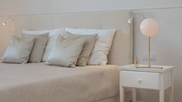 Un lit bien fait, avec une tête de lit et des oreillers de couleur claire, une table de chevet avec une lampe et un tiroir.