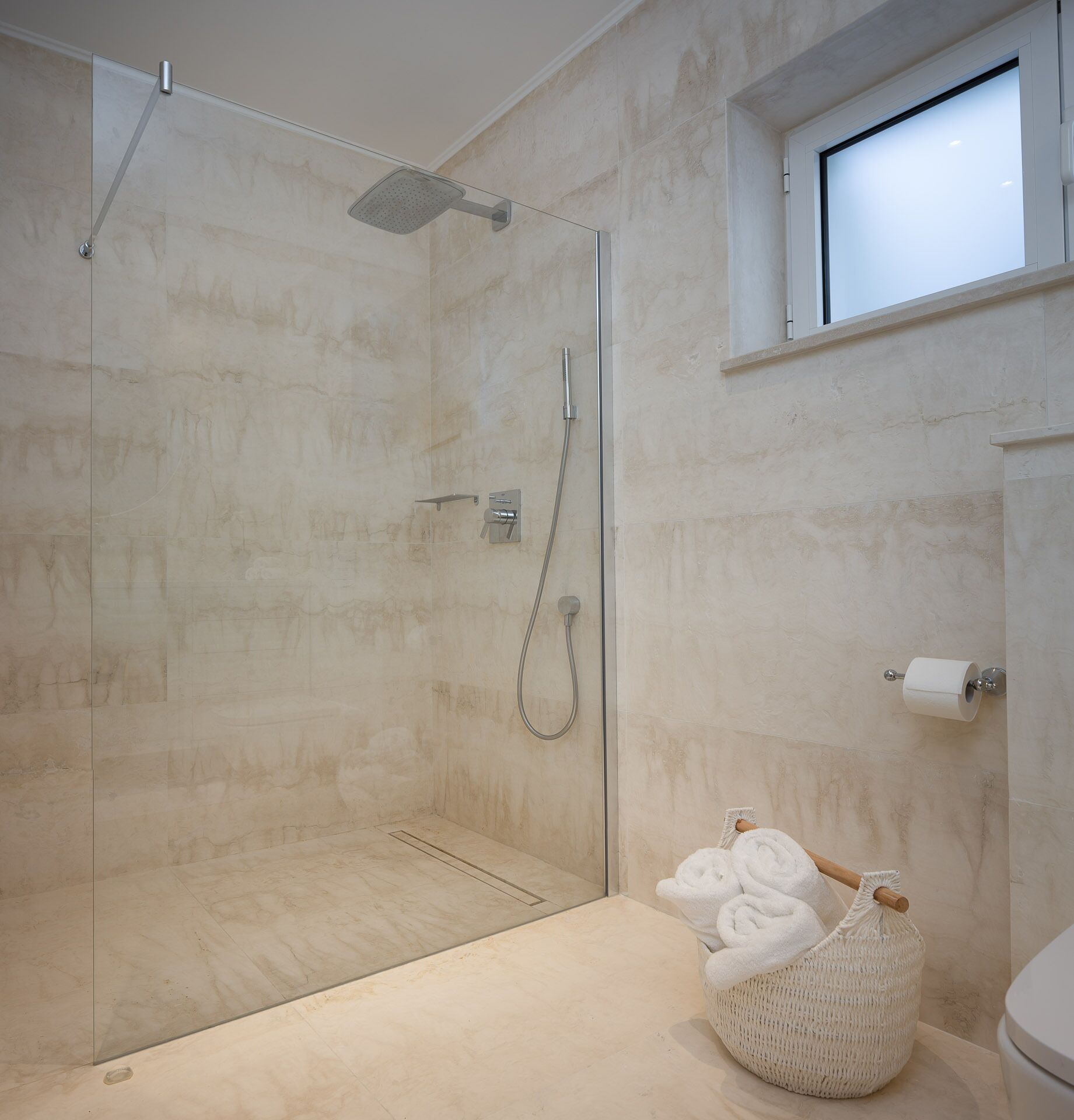 A modern bathroom with a glass-enclosed shower, a toilet, and a small window.