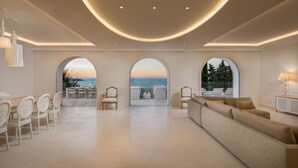 A spacious living room with a large sofa, a dining area with chairs, and three arched windows offering views of the sea. - Luxury Villa Dance Forever with Pool (Primosten)
