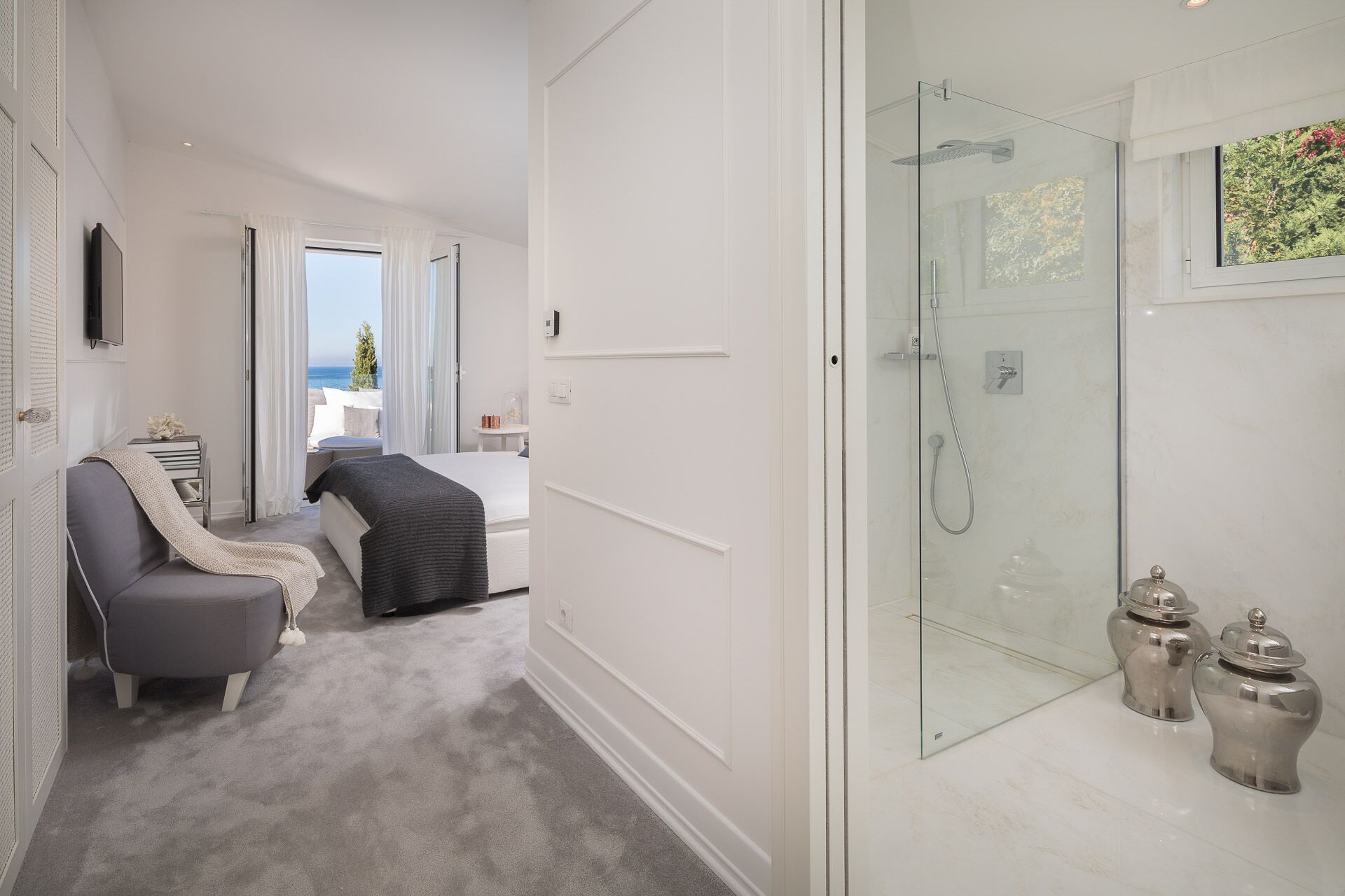Habitación de hotel con cama, sofá, ducha con mampara de vidrio y vista al mar.