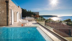 A pool area with a view of the sea, stone walls, and a glass balustrade. - Luxury Villa Dance Forever with Pool (Primosten)