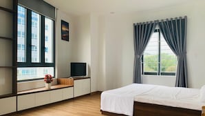 A modern hotel room with a large bed, a TV on a wooden console, a window with curtains, and a view of buildings outside. - Rang Dong hotel (Hue)