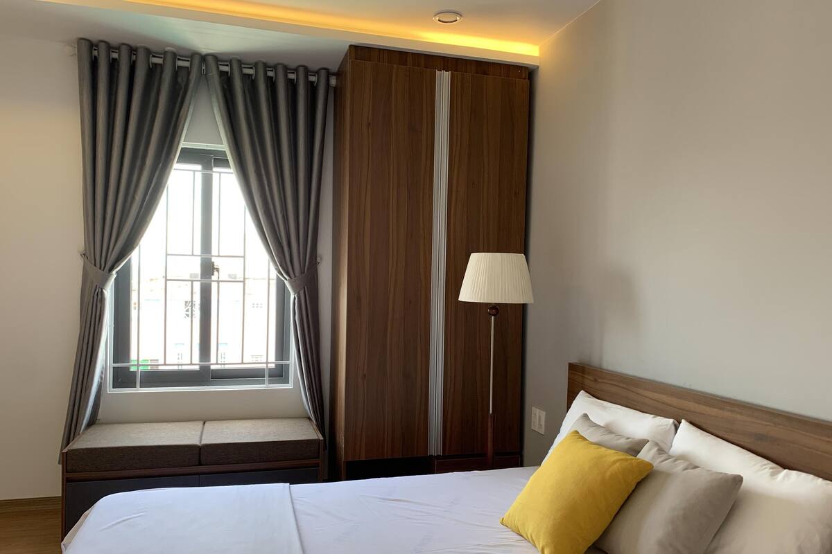 A hotel room with a bed, a window with curtains, a bedside lamp, and a wardrobe.