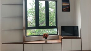 A room with a large window, a flat-screen TV on a wooden stand, and a small table with a potted plant. - Rang Dong hotel (Hue)