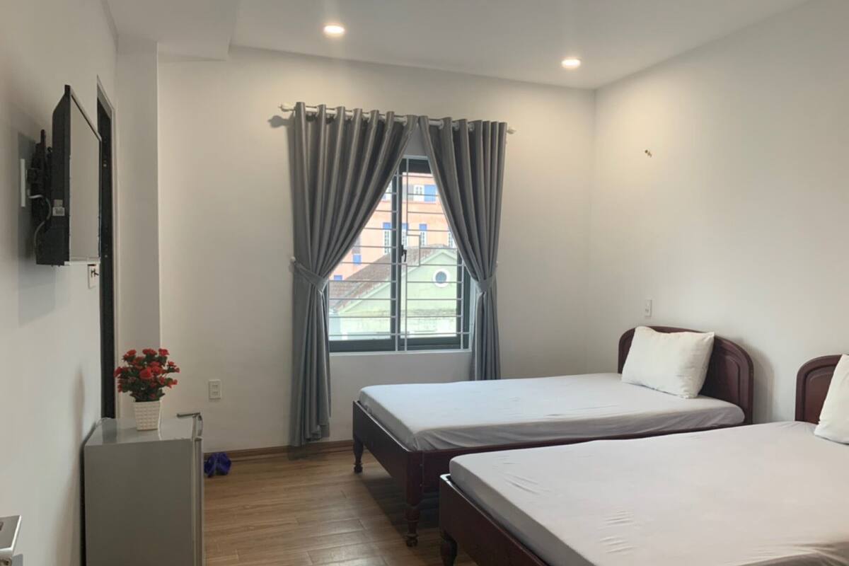 A bedroom with two beds, a small desk, a television, and a window with curtains.