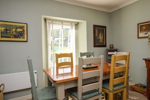 A dining area with a wooden table and chairs, a window with blinds, and framed artwork on the walls.