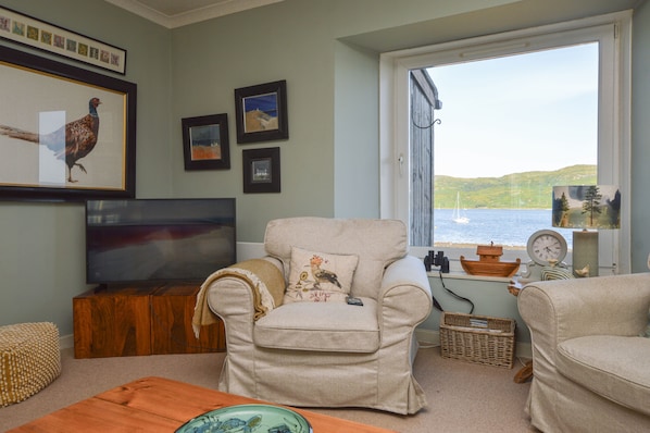 A living room with a television, framed artwork, and a view of the sea.