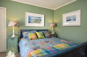 A bedroom with a bed, two bedside tables, two lamps, and two framed pictures on the wall.