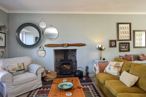 A cozy living room with a fireplace, a round mirror, and a wooden table.
