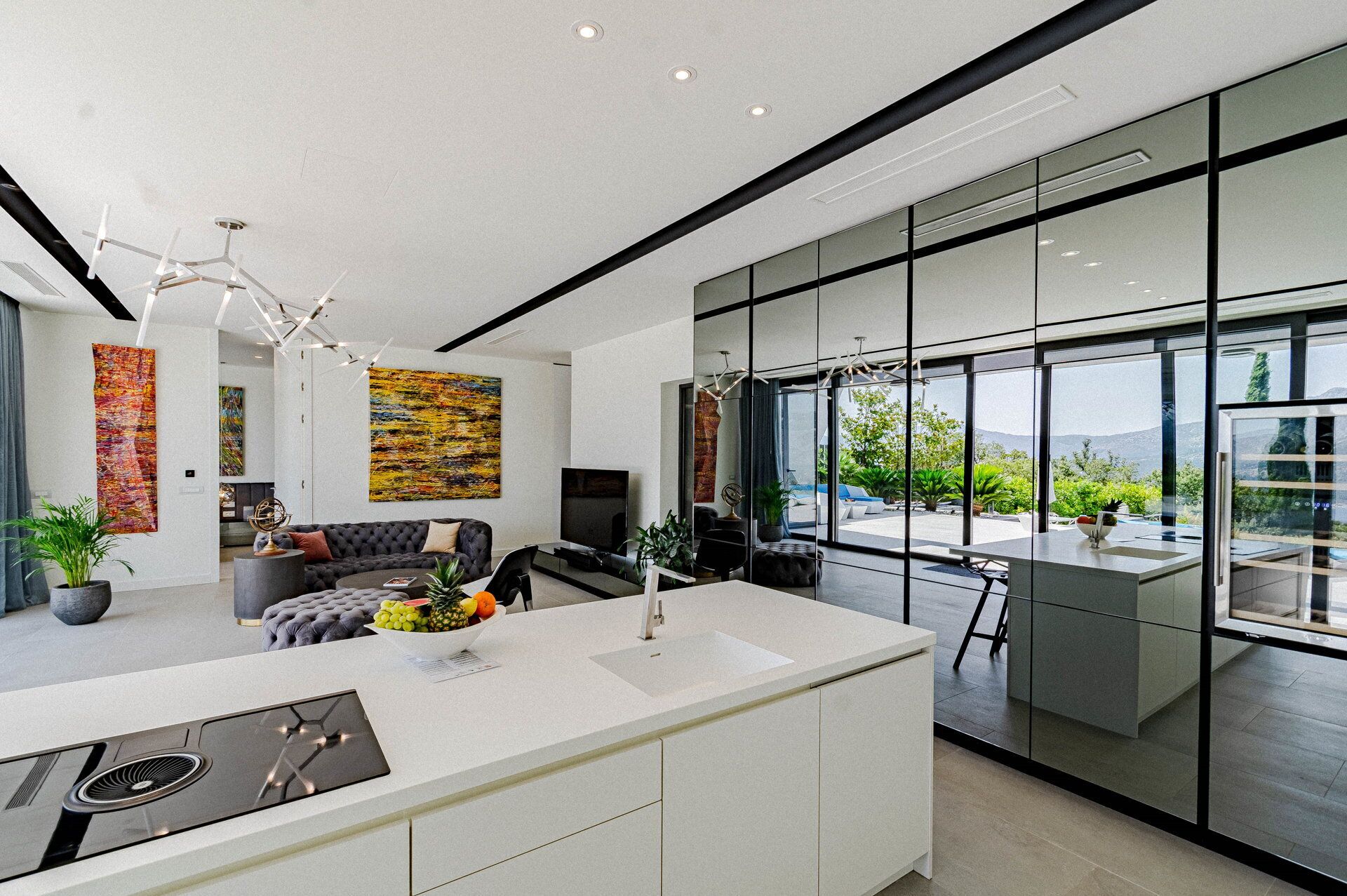 Una cocina moderna con una isla central, ventanas amplias y una sala de estar con sofá y televisor.