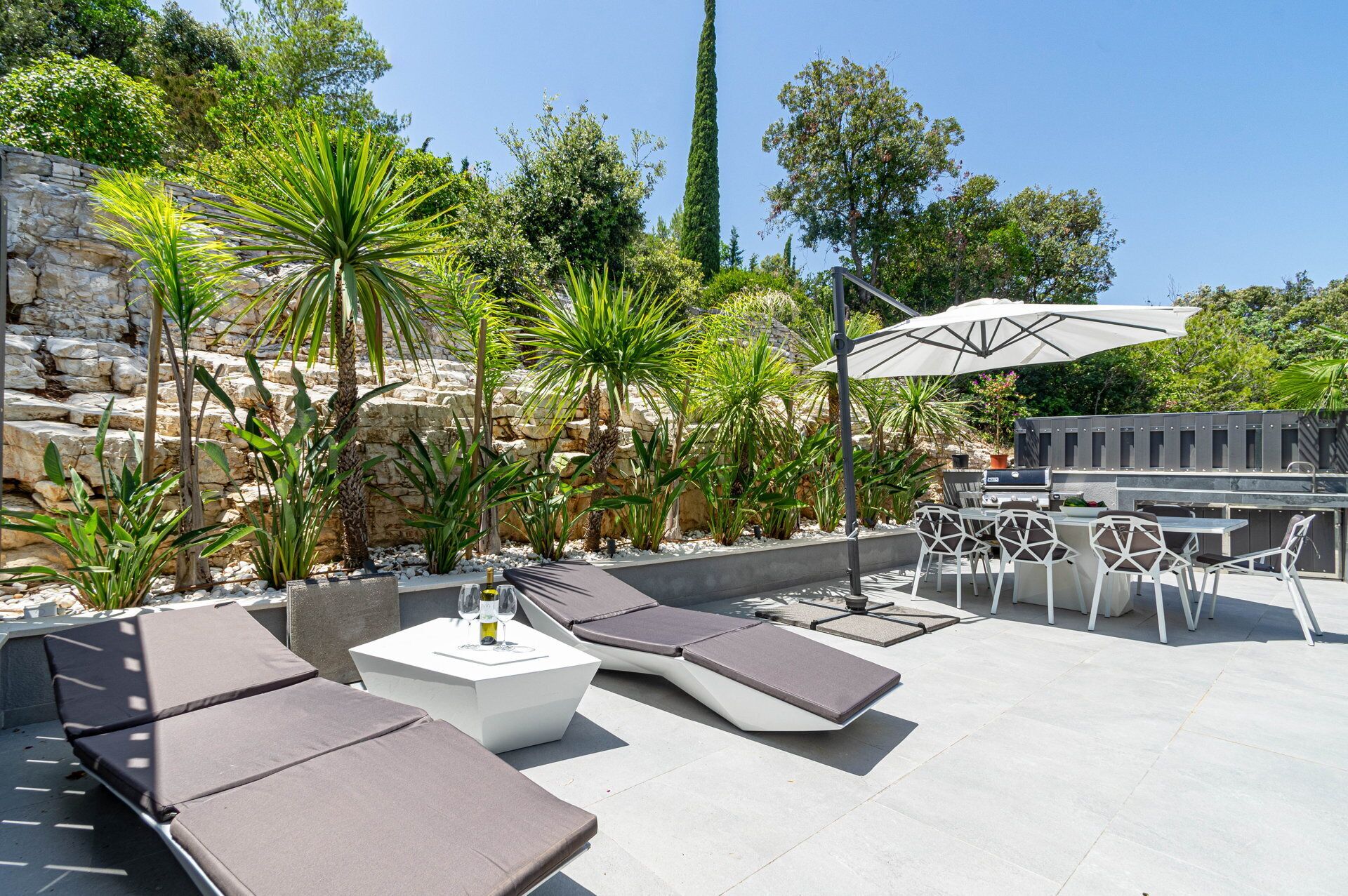 An outdoor patio with lounge chairs, a barbecue grill, and a stone wall backdrop.