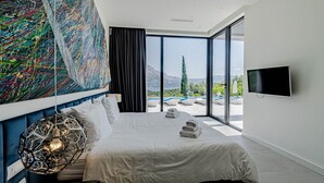 Une chambre moderne avec un grand lit, une télévision et une vue sur une piscine et des montagnes.
