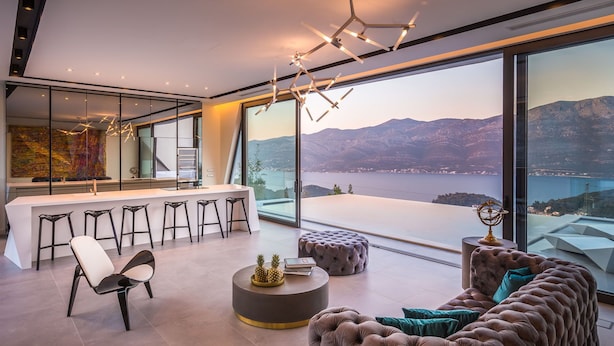 Un intérieur moderne comprenant un bar, des espaces pour s’asseoir et une grande fenêtre offrant une vue panoramique sur un lac et des montagnes.