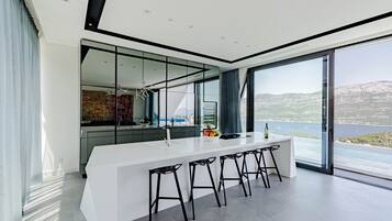 A modern kitchen with a large island, black bar stools, and a view of the sea.