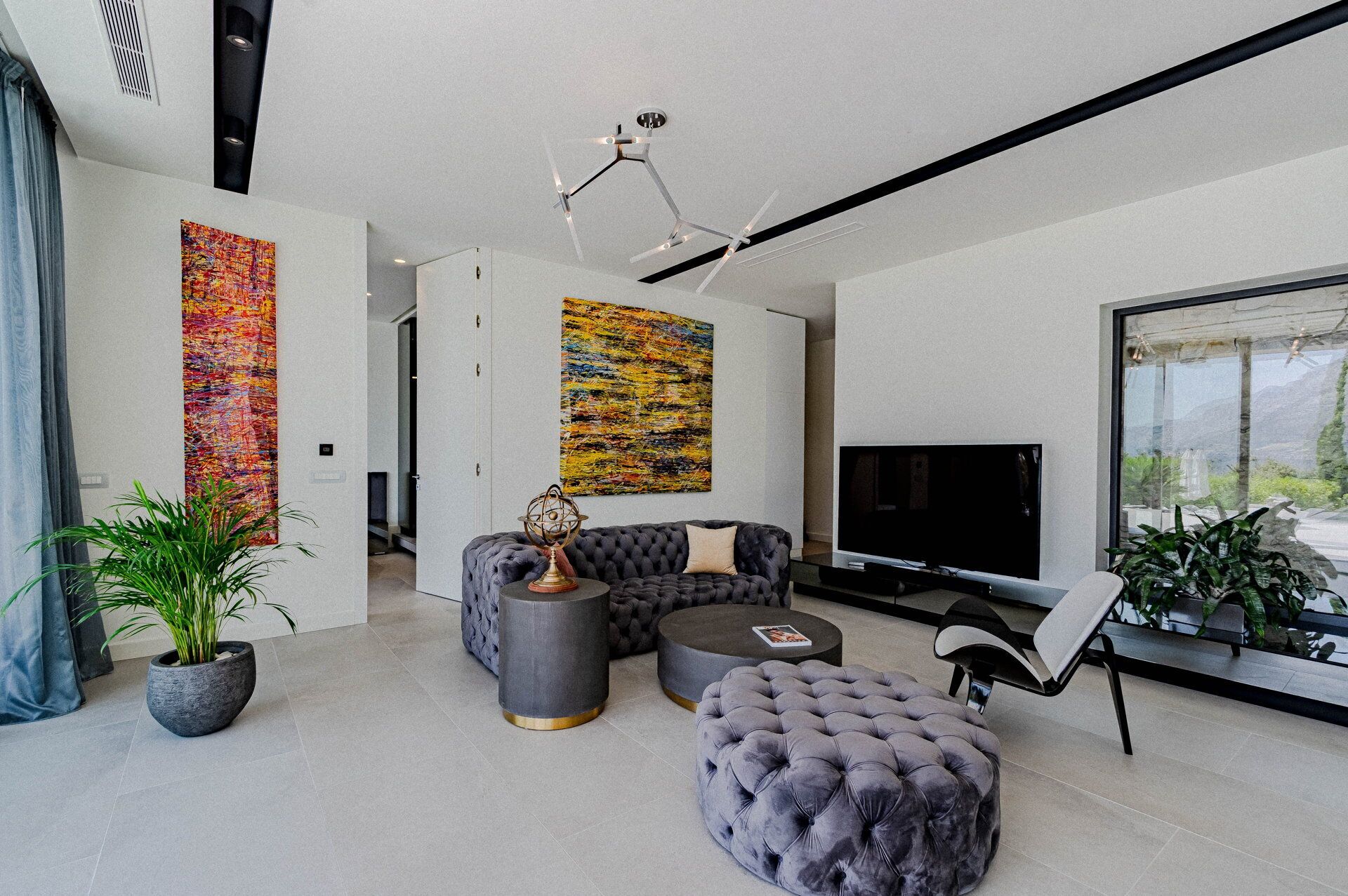 Una sala moderna con un sofá modular, un reposapiés redondo, un televisor y dos cuadros abstractos.