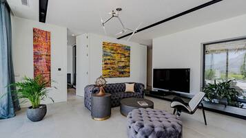 Una sala moderna con un sofá modular, un reposapiés redondo, un televisor y dos cuadros abstractos.