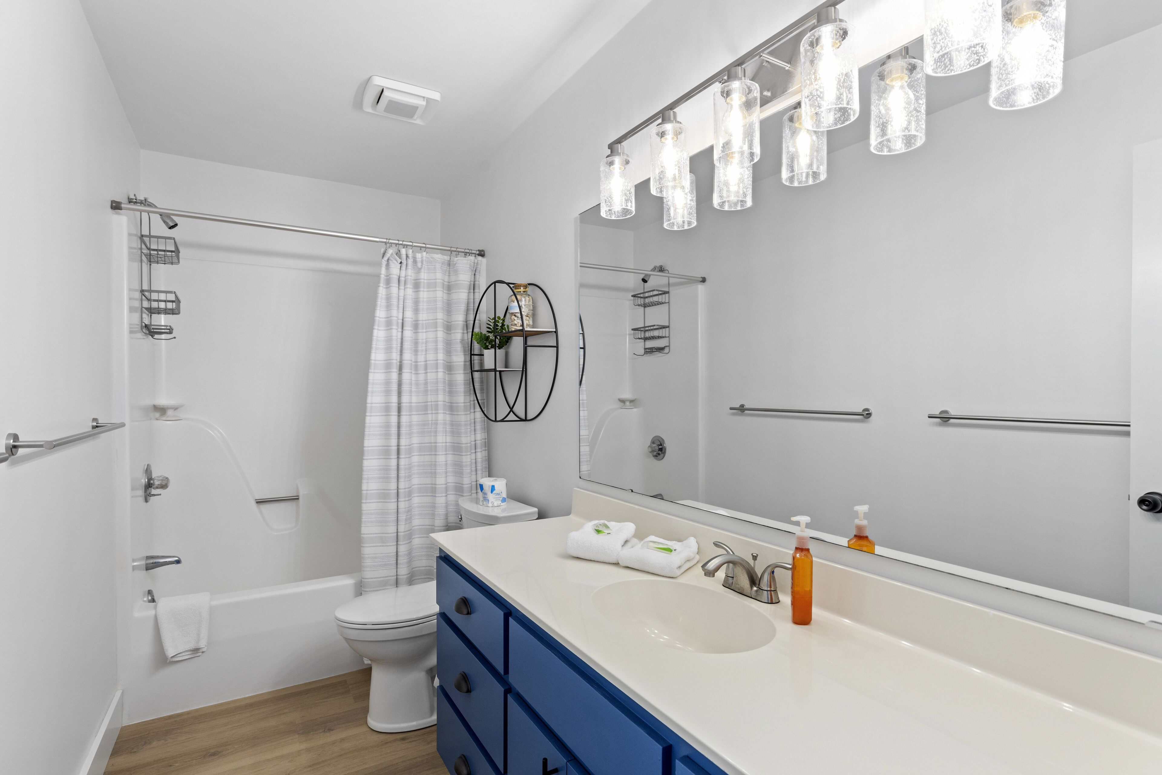 A modern bathroom with a white bathtub, a large mirror, and a white sink with blue cabinets.