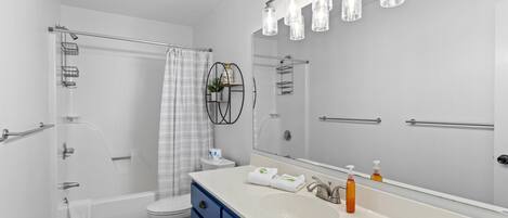 A modern bathroom with a white bathtub, a large mirror, and a white sink with blue cabinets.