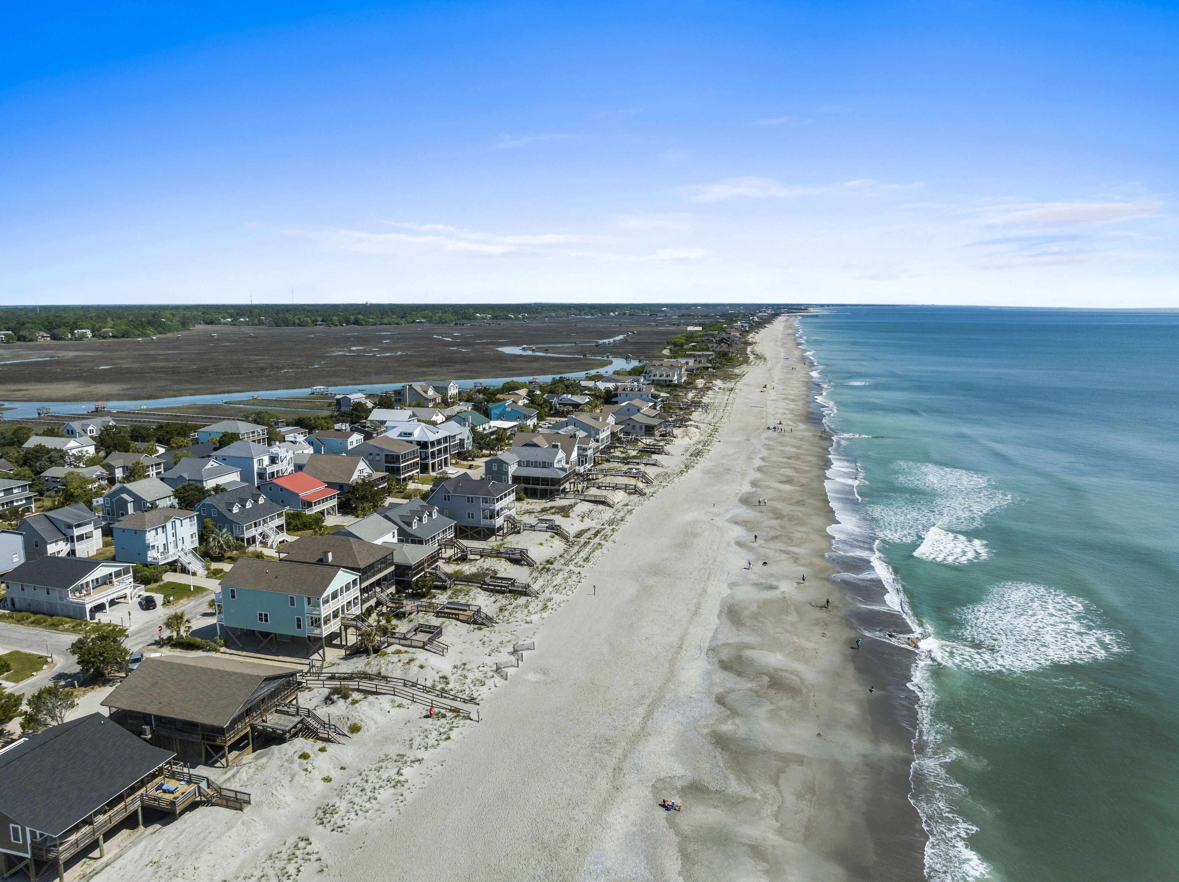 A coastal residential area with houses along the beach, a clear sky, and a view of the ocean.