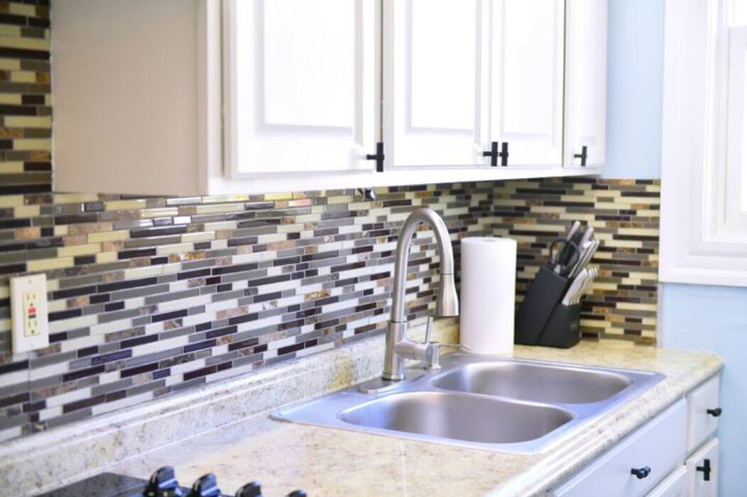 A kitchen with a double sink, white cabinets, and a mosaic tile backsplash.