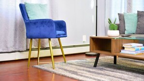 A modern living room with a blue velvet chair, a wooden coffee table with books, and a green cactus on a side table. - Cozy apartment 3rd 10min Walk Downtown | City View (Providence)