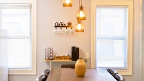 A dining area with a wooden table, two chairs, a vase, and a coffee station with a coffee machine and cups. - Cozy apartment 3rd 10min Walk Downtown | City View (Providence)