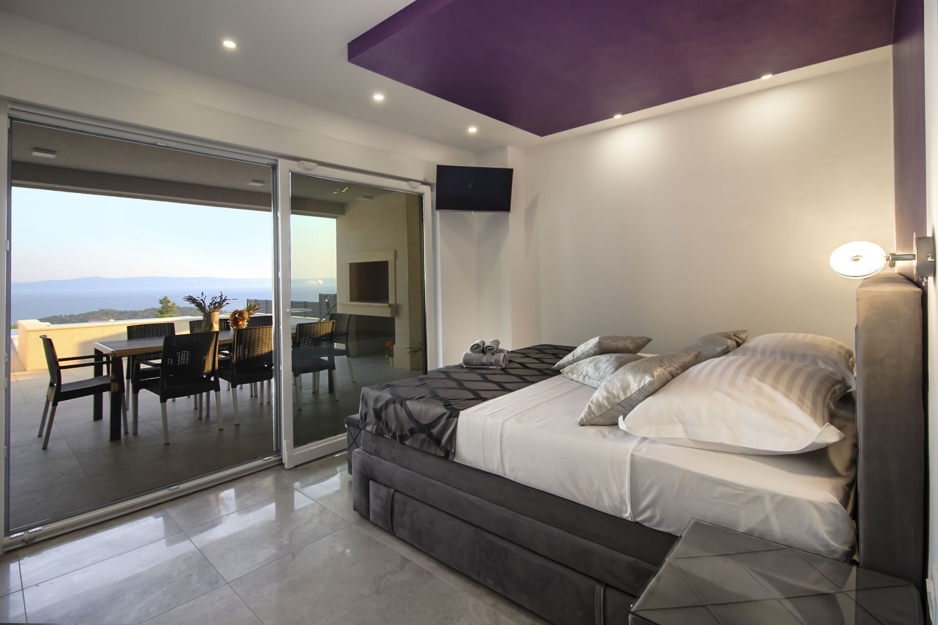 Un dormitorio moderno con cama, televisor y balcón con vistas.