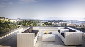 Terraza en la azotea con mobiliario de mimbre blanco, barandilla de cristal y vistas a la ciudad.
