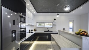 Una cocina moderna con un refrigerador de acero inoxidable, un horno empotrado y un dispensador de agua. Hay una isla grande con un lavamanos y una ventana encima.