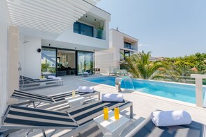 A modern outdoor pool area with lounge chairs and a glass-enclosed patio. - Luxury Villa Luna with Swimming Pool (Sutivan)