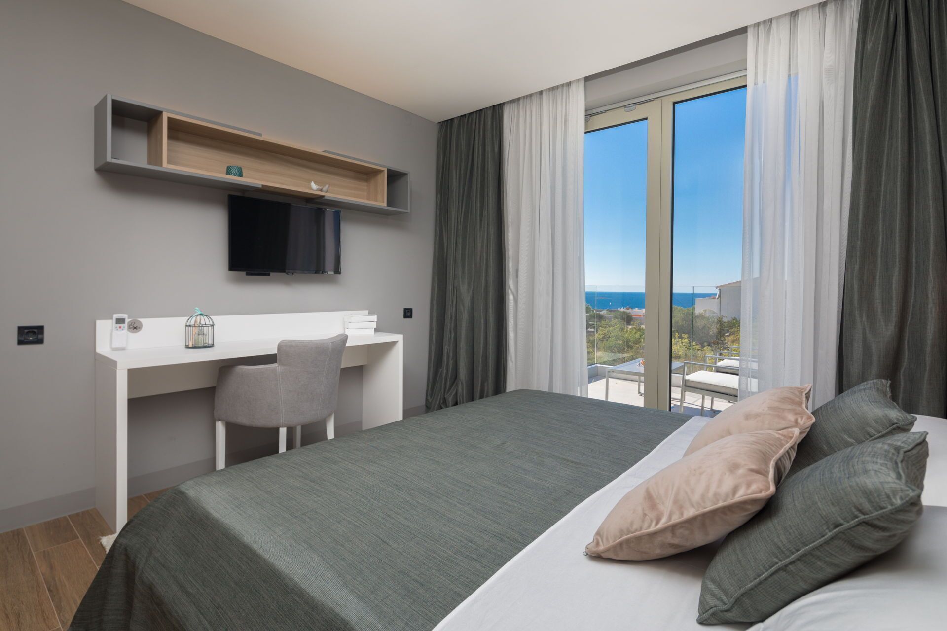 A modern hotel room with a bed, a desk, a chair, and a TV.